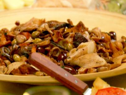 Warm salad of mushrooms and speck with green and black olives and oregano leaves.