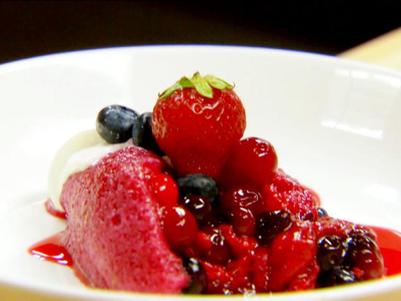 Summer berry pudding with whipped cream, raspberries, blackberries, and blueberries is topped with a strawberry.