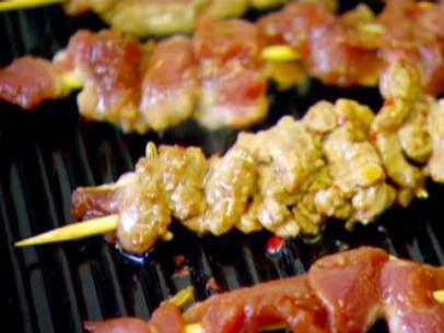 Spiced skewered lamb cooks on a grill with dried red chile flakes. 