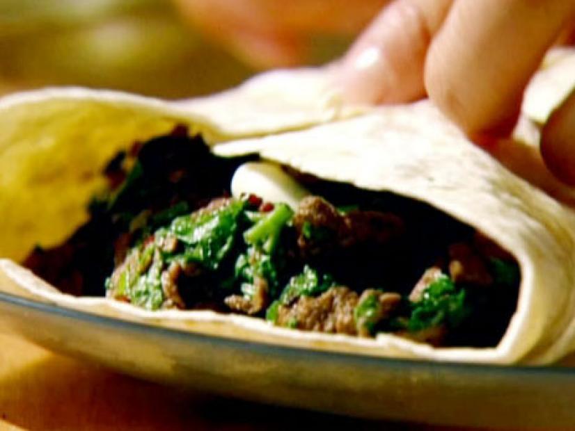 Spiced beef stir fry topped with spring onion and coriander is wrapped in a tortilla shell.