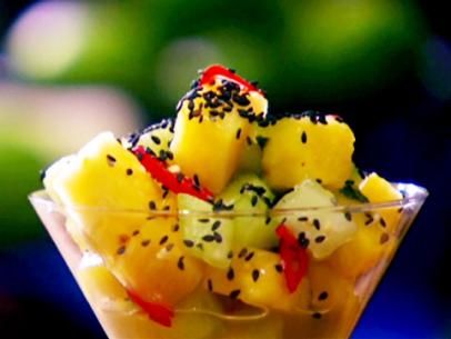 Tropical fruit salad with pineapple, mango, honeydew melon, Thai basil, cilantro is garnished with black sesame seeds.