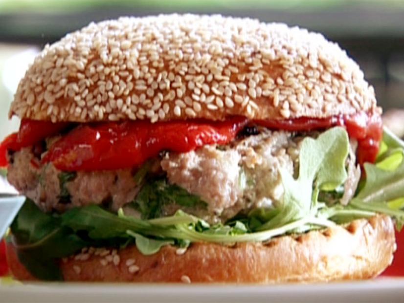 LA Burger is layered with ground pork, arugula leaves, and roasted peppers on hamburger bun with sesame seeds.