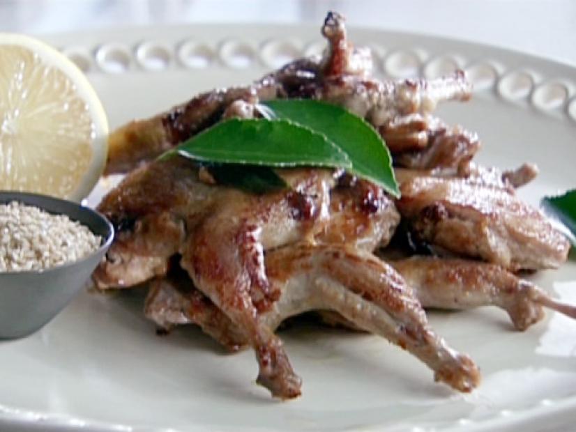 Barbecued quail is served with a side of spiced sea salt and half of a lemon. Bay leaves are used to garnish the quail.