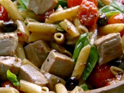 Chunks of tuna steak, cherry tomatoes, olives, and basil leaves are mixed into a bowl of penne pasta.