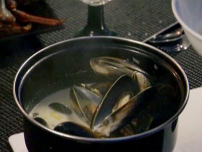 Mussels cook in a pot with a white wine sauce and leeks.