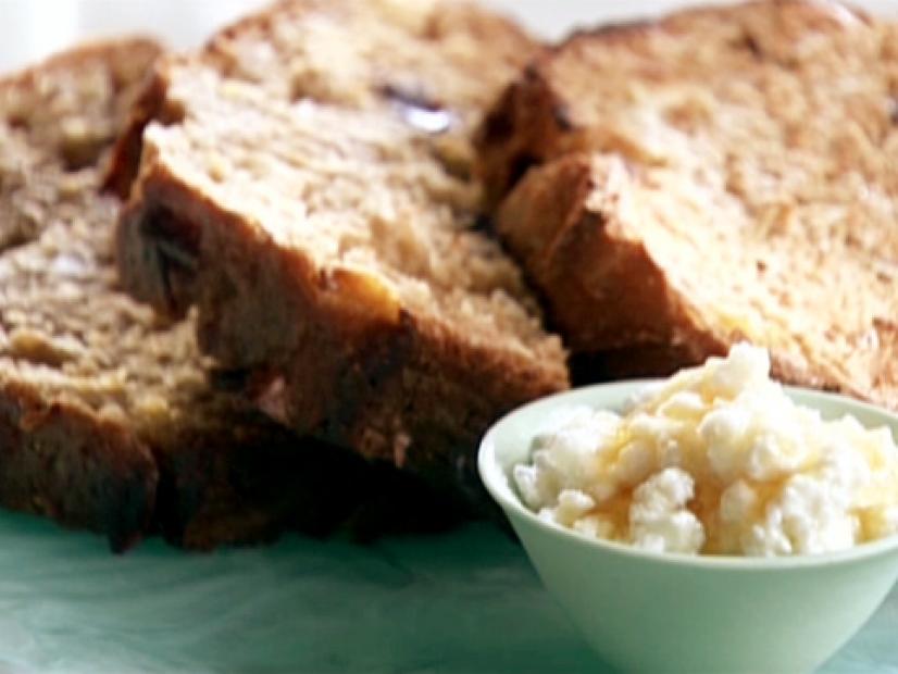 Slices of apple, dried cherry, and almond loaf is served with a side of ricotta and drizzled honey.