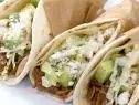 Carne asada tacos with green salsa is wrapped in brown paper.