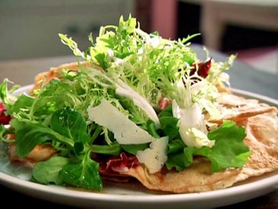 A salad on a bed of flatbread crackers and topped with Pecorino shavings