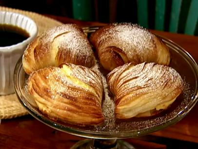 A serving dish with a sfogliatella pastry made to look like leaves. This dish has many layers of crispy dough leaves and filled with ricotta cheese. Powdered sugar has been added to the top.