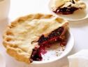 A blueberry pie with thick golden brown crust is served in a glass pie dish.