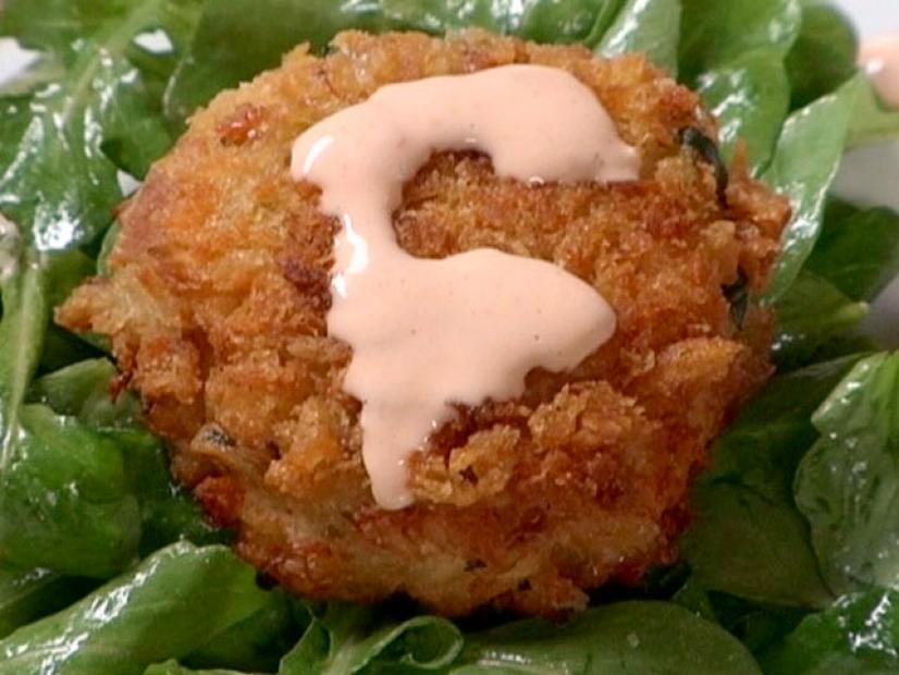 A crispy crab cake topped with a sweet and tangy remoulade sauce is served on a bed of salad greens.