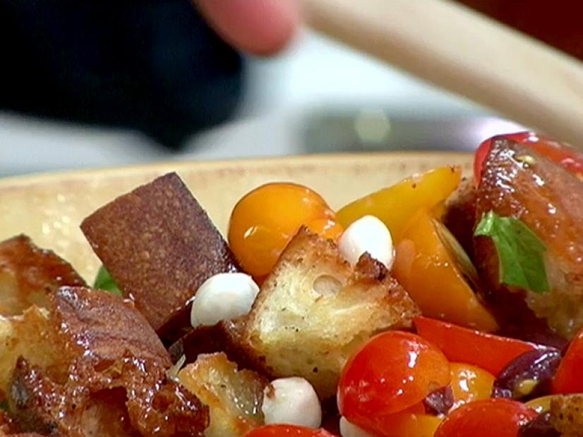 A close up of a tomato and garlic crouton salad. The salad has cherry, grape, and pear tomatoes, mozzarella cheese, basil, kalamata olives and garlic croutons. A red wine vinaigrette has been poured over the salad.
