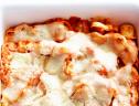 A close up of a dish of cheesy baked tortellini that has been topped with smoked mozzarella and grated parmesan cheese.