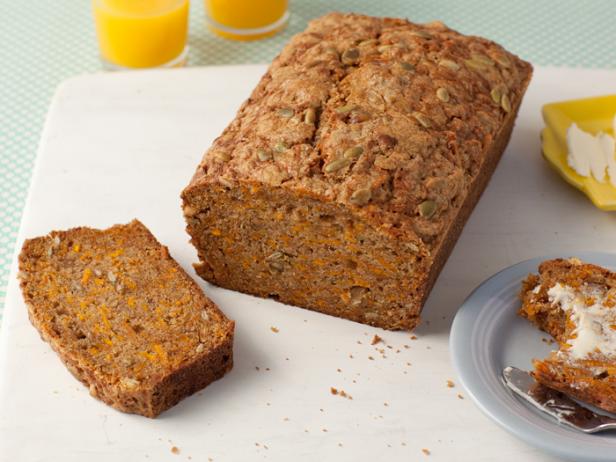 A loaf of Brown Pumpkin Bread with one slice removed that is placed on a plain white surface
