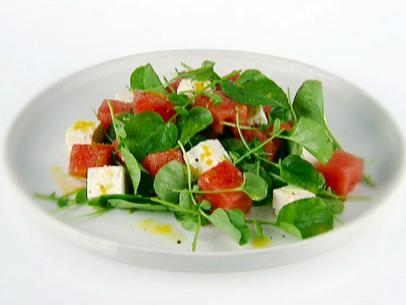A plate with a salad of watermelon, watercress, and feta cheese topped with a dressing of lemon zest, lemon juice, and olive oil.