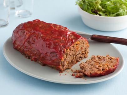 A meatloaf with a slice removed on a plain oval gray plate