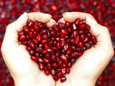 Hands holding pomegranate arils in the shape of a heart.