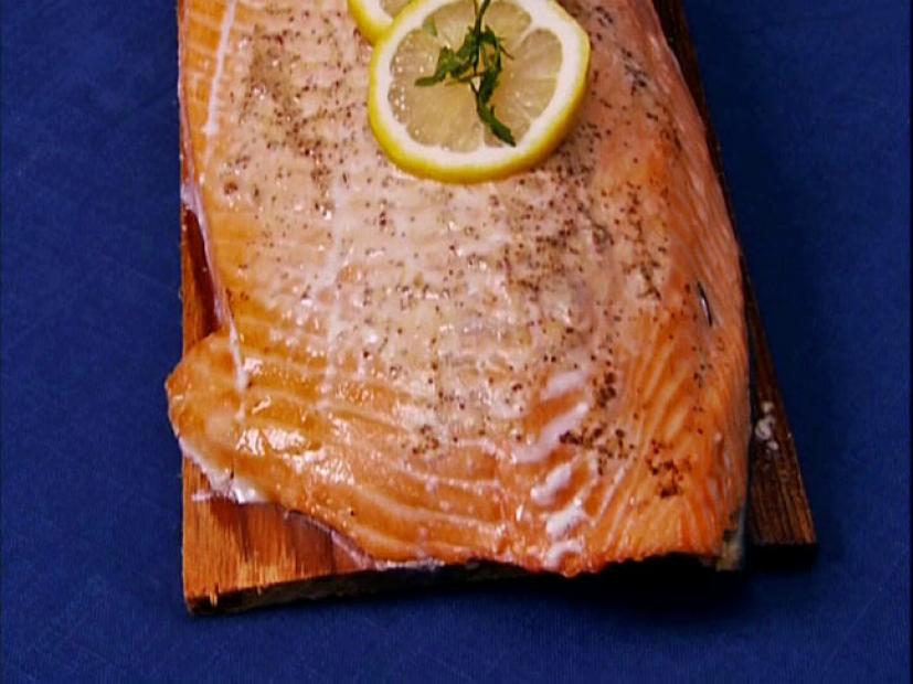 A piece of salmon on a cedar plank topped with a slice of lemon