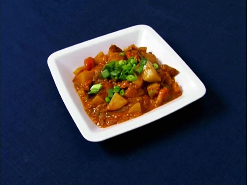 Turtle Stew topped with chopped onions in a simple square white dish placed on a dark blue surface