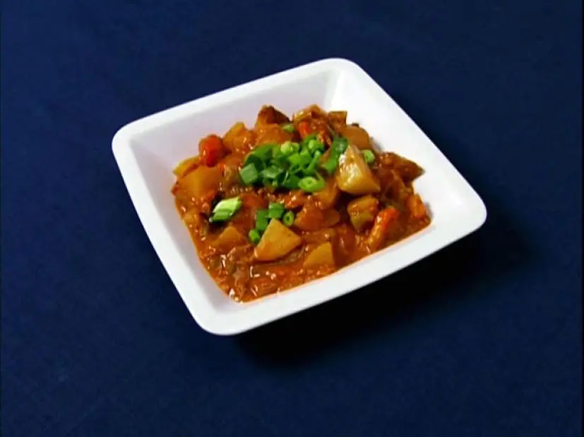 Turtle Stew topped with chopped onions in a simple square white dish placed on a dark blue surface