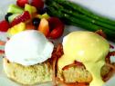 Eggs benedict is served wtih fresh fruit and asparagus.