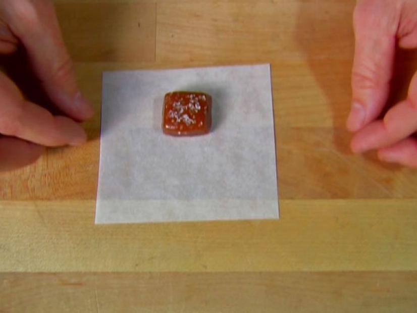 A square piece of dark caramel sprinkled with salt is placed in the center of a square piece of wax paper.