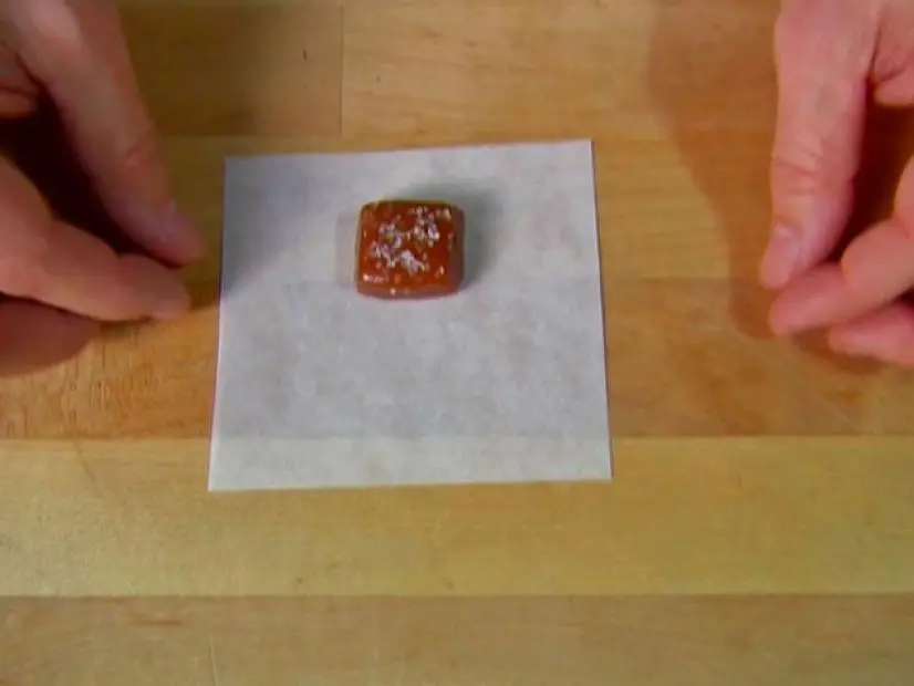 A square piece of dark caramel sprinkled with salt is placed in the center of a square piece of wax paper.