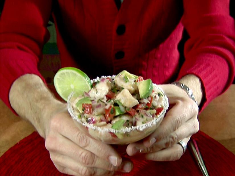 Hands hold a salt rimmed margarita glass that has been filled with ceviche made from catfish cubes that were marinated with citrus juices and zests. The fish was combined with a salad of seeded and minced jalapeno, diced red onion, seeded and diced tomato, sliced garlic, chopped fresh cilantro, chopped fresh oregano, and a diced avocado.
