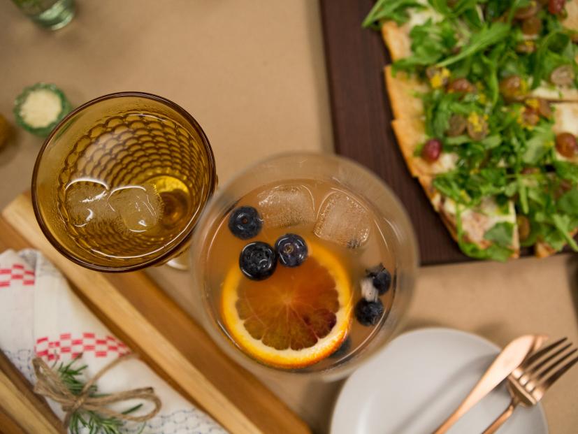 A Blood Orange Soda Sangria towers over a Ricotta, Arugula, Grape, Pine Nut, and Lemon Zest Pizza, as seen on Cooking Channel's Dinner At Tiffani's, Season 1.