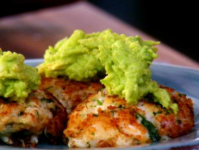 A close up of spicy crab cakes that have been topped with guacamole.