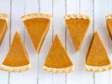 7 slices of homemade pumpkin pie in row sitting on white wooden table