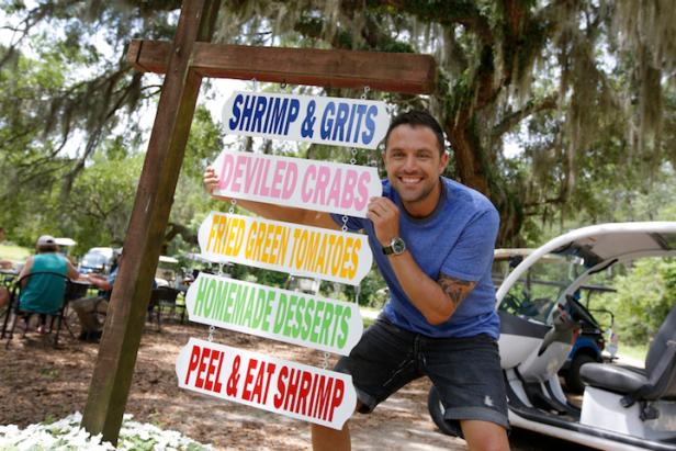 Host Sabin Lomac Posing Next to the hanging signage out front of Lucy Bell's in Daufuskie Island, South Carolina as seen on Cooking Channel's Seaside Snacks and Shacks, Season 1.